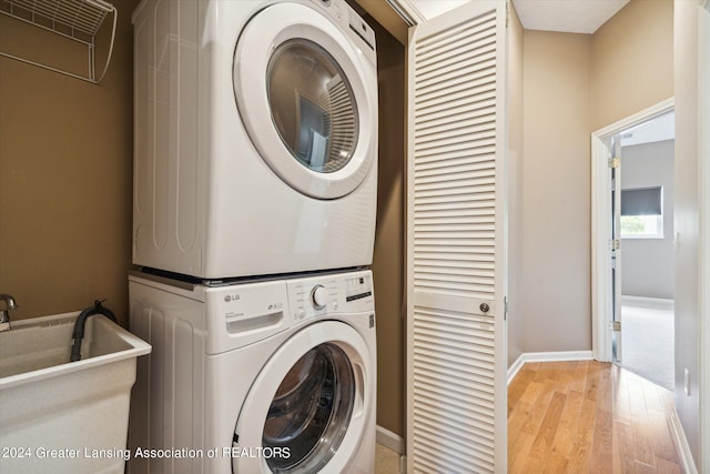 laundry room with sink, light hardwood / wood-style floors, and stacked washer / drying machine