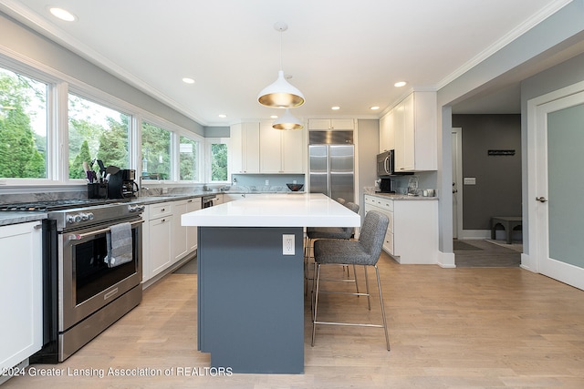 kitchen with pendant lighting, high end appliances, white cabinetry, a center island, and light hardwood / wood-style floors