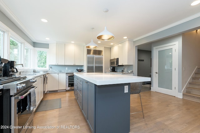 kitchen featuring high end appliances, wine cooler, a center island, hanging light fixtures, and white cabinetry