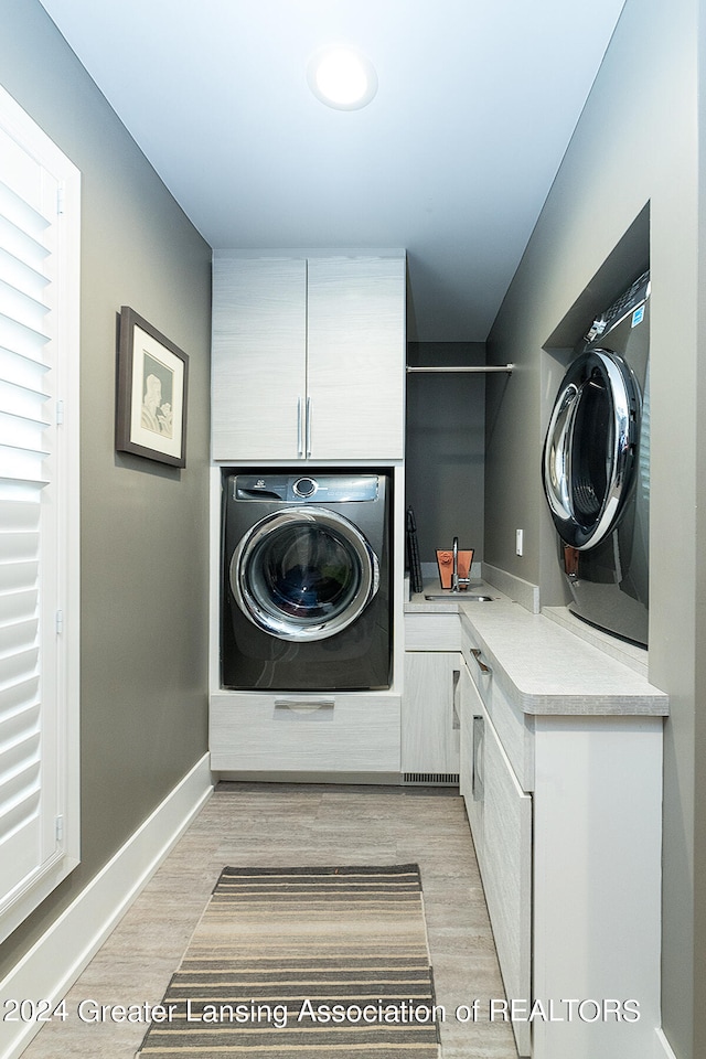 laundry area with washer / clothes dryer, light wood-type flooring, and cabinets