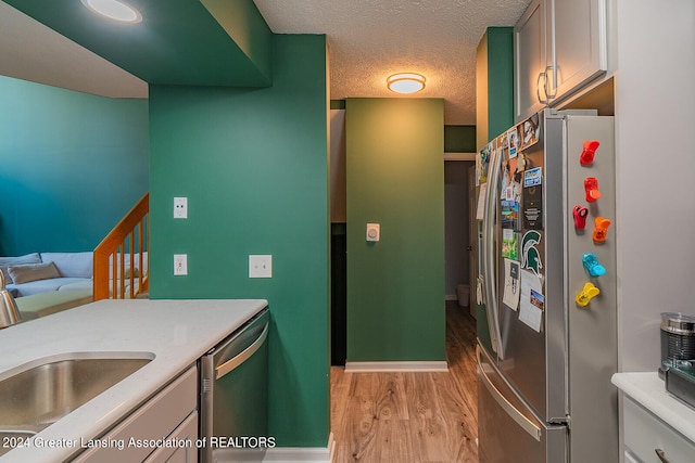 kitchen with appliances with stainless steel finishes, sink, light hardwood / wood-style flooring, and a textured ceiling