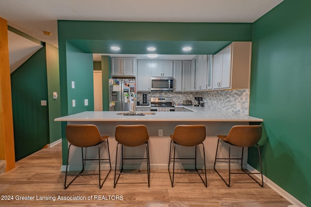 kitchen featuring sink, appliances with stainless steel finishes, light hardwood / wood-style flooring, tasteful backsplash, and kitchen peninsula