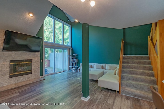 living room with a textured ceiling, stairway, wood finished floors, and a glass covered fireplace