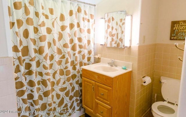 bathroom with curtained shower, toilet, vanity, tile walls, and wainscoting