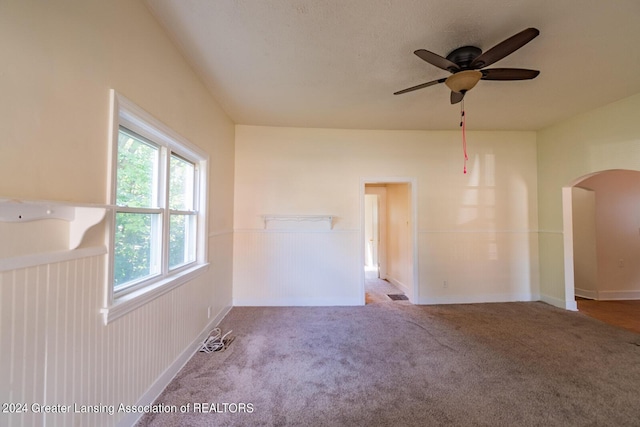 unfurnished room featuring visible vents, arched walkways, a ceiling fan, wainscoting, and carpet flooring