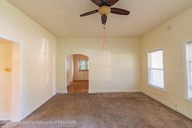 carpeted empty room featuring lofted ceiling, arched walkways, a ceiling fan, and wainscoting