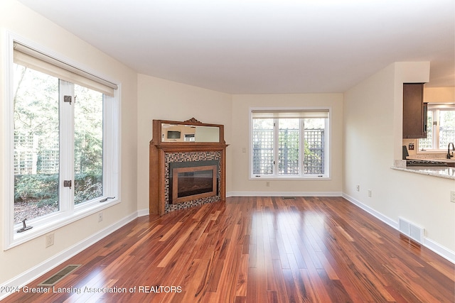 unfurnished living room featuring a tiled fireplace, plenty of natural light, and dark hardwood / wood-style floors