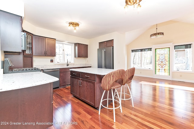 kitchen with sink, appliances with stainless steel finishes, hardwood / wood-style floors, a kitchen island, and vaulted ceiling