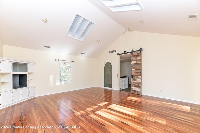 unfurnished living room featuring light wood-type flooring, a barn door, a skylight, and high vaulted ceiling