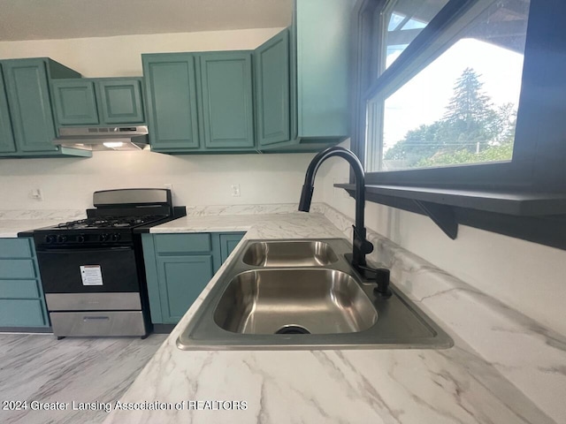 kitchen featuring stainless steel gas range, green cabinetry, light stone counters, and sink