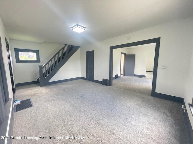 carpeted empty room featuring visible vents, baseboards, and stairs