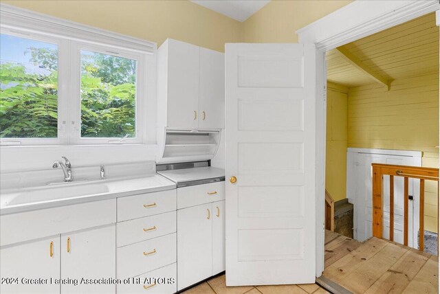 kitchen with sink, beamed ceiling, white cabinetry, and light tile patterned flooring