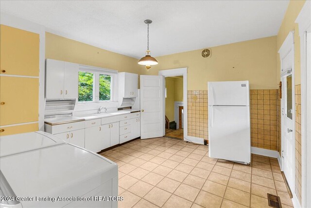 kitchen featuring light tile patterned floors, hanging light fixtures, tile walls, white cabinetry, and white refrigerator