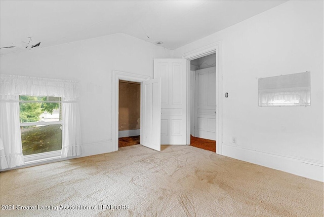 unfurnished bedroom with lofted ceiling, a closet, and light colored carpet