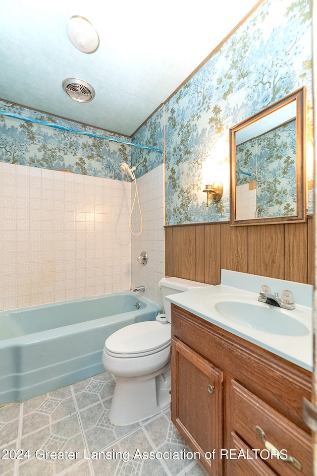 full bathroom featuring vanity, wood walls, tiled shower / bath combo, tile patterned flooring, and toilet