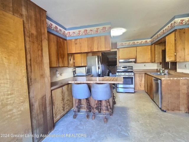 kitchen with ventilation hood, sink, a breakfast bar area, and stainless steel appliances