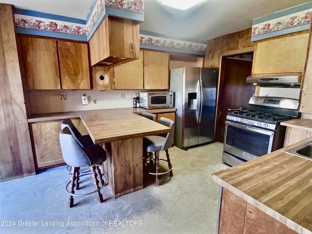 kitchen featuring a breakfast bar, kitchen peninsula, exhaust hood, and stainless steel appliances