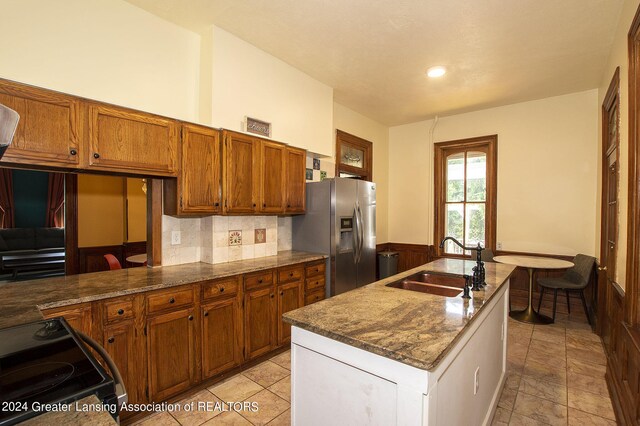 kitchen featuring stainless steel fridge, kitchen peninsula, sink, black range with electric cooktop, and stone counters