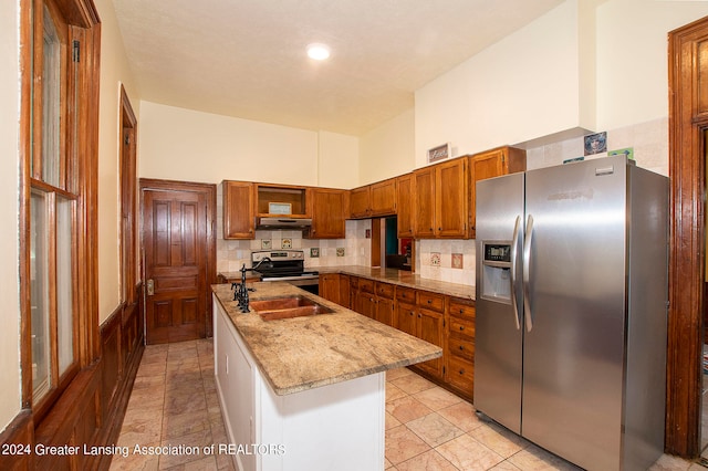 kitchen with appliances with stainless steel finishes, kitchen peninsula, sink, decorative backsplash, and light stone counters