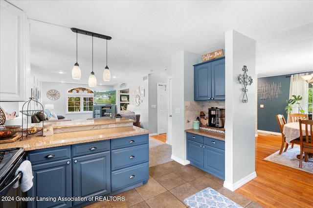 kitchen with decorative light fixtures, light hardwood / wood-style flooring, backsplash, blue cabinetry, and black stove