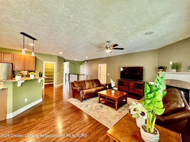 living room with a textured ceiling, wood-type flooring, ceiling fan, and a tile fireplace