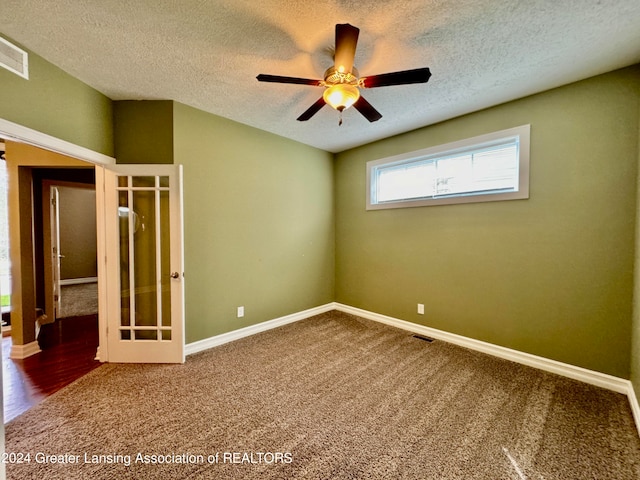 unfurnished room with a textured ceiling, dark carpet, and ceiling fan