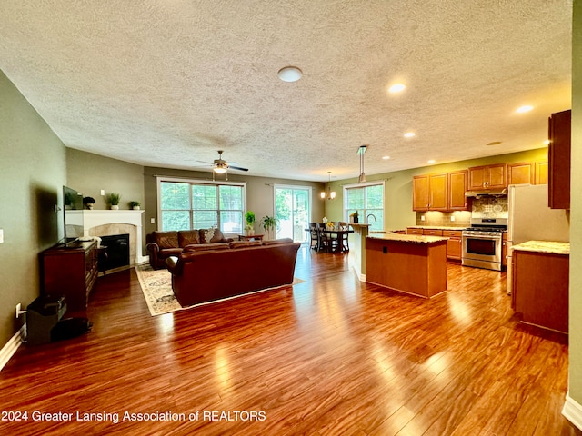 kitchen featuring a center island with sink, pendant lighting, gas stove, dark wood-type flooring, and ceiling fan