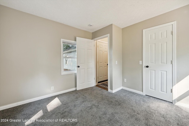 unfurnished bedroom with dark carpet and a textured ceiling