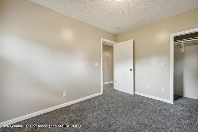 unfurnished bedroom with a textured ceiling, dark carpet, and a closet