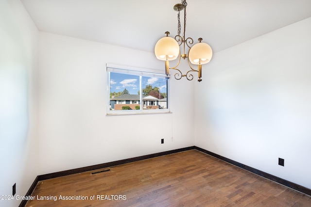 spare room with dark hardwood / wood-style floors and an inviting chandelier