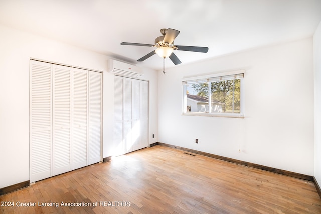 unfurnished bedroom featuring ceiling fan, two closets, light wood-type flooring, and an AC wall unit