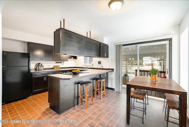 kitchen featuring a breakfast bar, extractor fan, black appliances, light tile patterned floors, and a center island