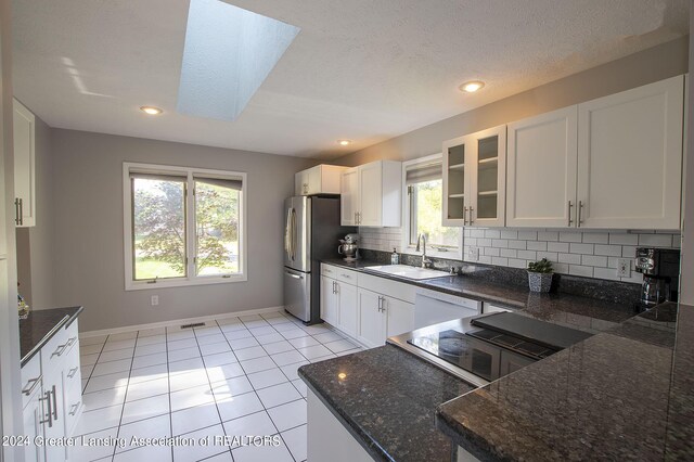 kitchen with a skylight, stainless steel refrigerator, sink, and white cabinets