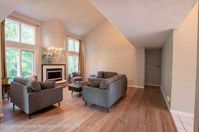 living room featuring a textured ceiling, a tiled fireplace, high vaulted ceiling, and light hardwood / wood-style floors