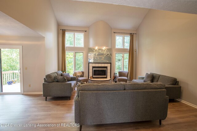 living room with a textured ceiling, high vaulted ceiling, hardwood / wood-style floors, and a tile fireplace