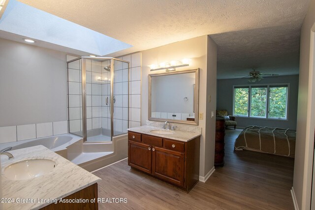 bathroom featuring a textured ceiling, shower with separate bathtub, vanity, hardwood / wood-style flooring, and a skylight