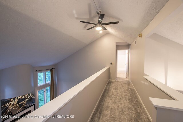 hall with lofted ceiling, carpet flooring, and a textured ceiling