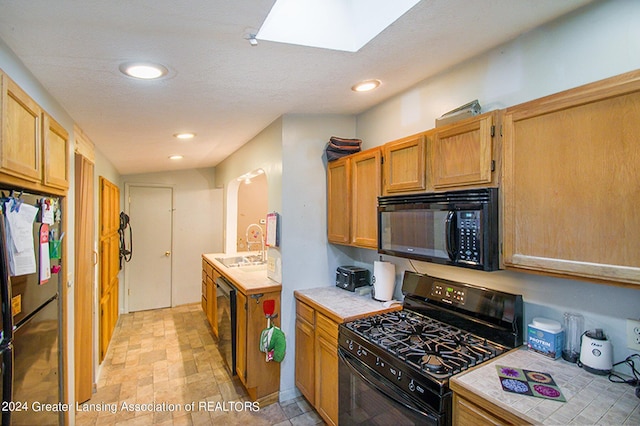 kitchen featuring a skylight, a sink, black appliances, stone finish floor, and tile counters