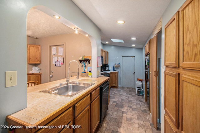 kitchen featuring arched walkways, stone finish flooring, black dishwasher, and a sink