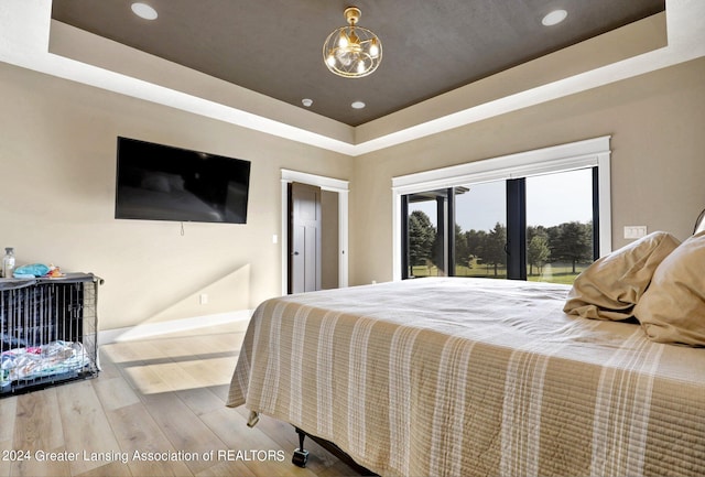 bedroom with a tray ceiling, a notable chandelier, and light hardwood / wood-style floors