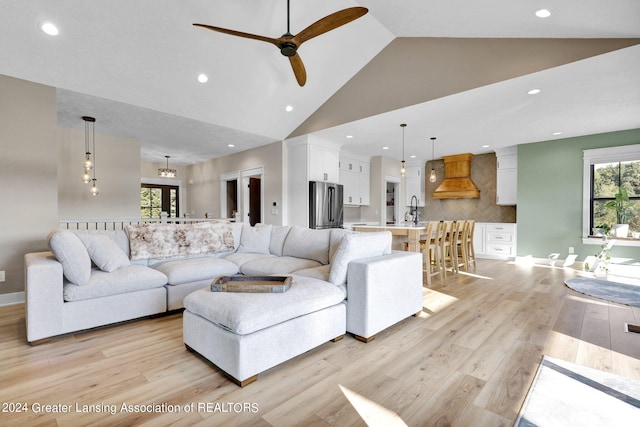 living room featuring light wood-type flooring, high vaulted ceiling, sink, and ceiling fan