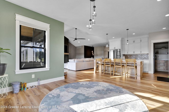 living room with ceiling fan, light wood-type flooring, and vaulted ceiling