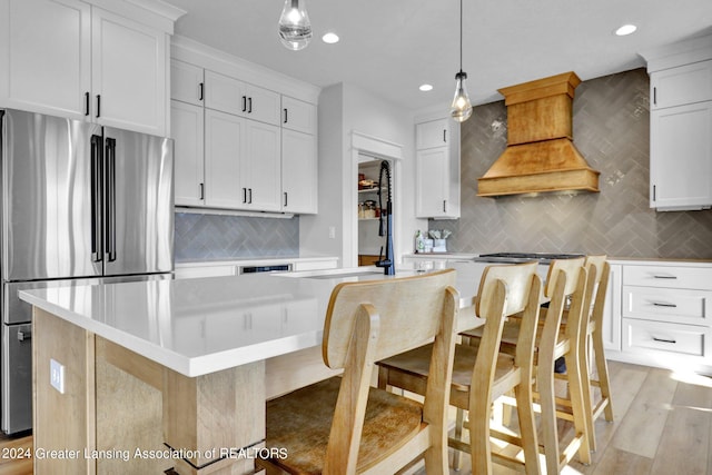 kitchen with light wood-type flooring, stainless steel fridge, a kitchen island, hanging light fixtures, and custom range hood