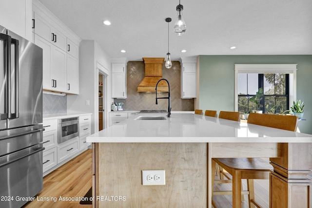 kitchen featuring light wood-type flooring, white cabinetry, a kitchen bar, an island with sink, and appliances with stainless steel finishes