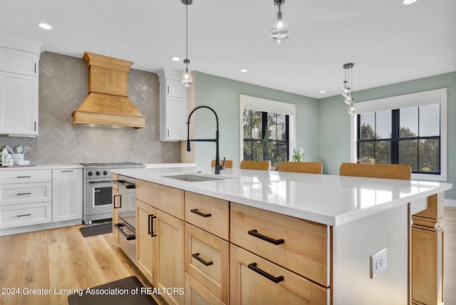 kitchen with light wood-type flooring, sink, premium range hood, high end range, and a center island with sink