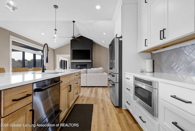 kitchen with vaulted ceiling, appliances with stainless steel finishes, light hardwood / wood-style floors, a brick fireplace, and white cabinetry