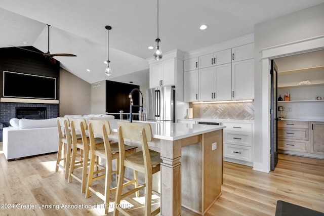 kitchen featuring a kitchen island with sink, a brick fireplace, ceiling fan, lofted ceiling, and white cabinets