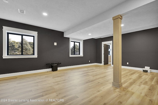 basement featuring light hardwood / wood-style flooring, a textured ceiling, and a healthy amount of sunlight