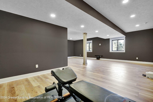 workout room with a textured ceiling, light hardwood / wood-style flooring, and decorative columns