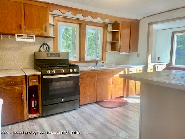 kitchen with light hardwood / wood-style floors, tasteful backsplash, tile countertops, stainless steel gas stove, and sink